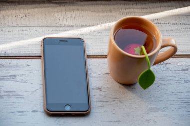 Bir fincan çay, ahşap bir masada telefon. Masa ve sandalyeler parlak bir odada. Çay ve telefon..