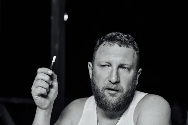 portrait of young grumpy bearded red hair man with sigaret horizontal. A man with a red beard smokes. The guy smokes an electronic cigarette. A man in a white T-shirt. Relaxation. Evening photo