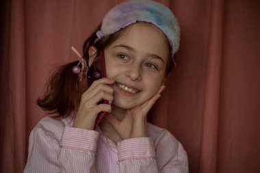 İnsanlar ve eğlence konsepti. Kırmızı ceketli bir kız selfie çekiyor. Evinde elinde telefon olan 9 yaşında bir kız. Pijamalı bir genç. Ev elbiseli küçük kız..