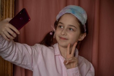 İnsanlar ve eğlence konsepti. Kırmızı ceketli bir kız selfie çekiyor. Evinde elinde telefon olan 9 yaşında bir kız. Pijamalı bir genç. Ev elbiseli küçük kız..