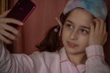İnsanlar ve eğlence konsepti. Kırmızı ceketli bir kız selfie çekiyor. Evinde elinde telefon olan 9 yaşında bir kız. Pijamalı bir genç. Ev elbiseli küçük kız..