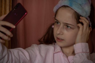İnsanlar ve eğlence konsepti. Kırmızı ceketli bir kız selfie çekiyor. Evinde elinde telefon olan 9 yaşında bir kız. Pijamalı bir genç. Ev elbiseli küçük kız..