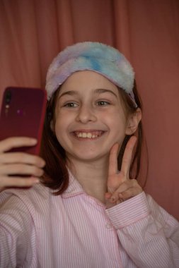İnsanlar ve eğlence konsepti. Kırmızı ceketli bir kız selfie çekiyor. Evinde elinde telefon olan 9 yaşında bir kız. Pijamalı bir genç. Ev elbiseli küçük kız..