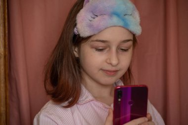 İnsanlar ve eğlence konsepti. Kırmızı ceketli bir kız selfie çekiyor. Evinde elinde telefon olan 9 yaşında bir kız. Pijamalı bir genç. Ev elbiseli küçük kız..