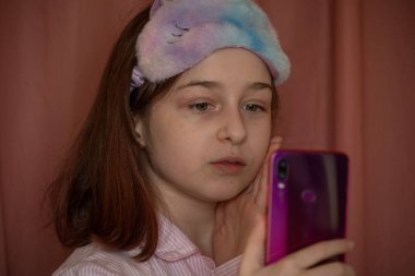 İnsanlar ve eğlence konsepti. Kırmızı ceketli bir kız selfie çekiyor. Evinde elinde telefon olan 9 yaşında bir kız. Pijamalı bir genç. Ev elbiseli küçük kız..