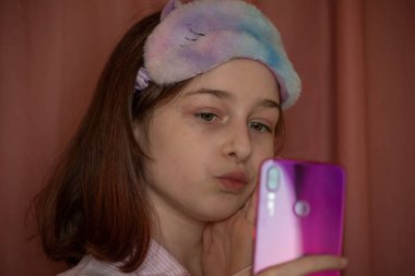 İnsanlar ve eğlence konsepti. Kırmızı ceketli bir kız selfie çekiyor. Evinde elinde telefon olan 9 yaşında bir kız. Pijamalı bir genç. Ev elbiseli küçük kız..