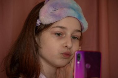 İnsanlar ve eğlence konsepti. Kırmızı ceketli bir kız selfie çekiyor. Evinde elinde telefon olan 9 yaşında bir kız. Pijamalı bir genç. Ev elbiseli küçük kız..