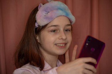 İnsanlar ve eğlence konsepti. Kırmızı ceketli bir kız selfie çekiyor. Evinde elinde telefon olan 9 yaşında bir kız. Pijamalı bir genç. Ev elbiseli küçük kız..