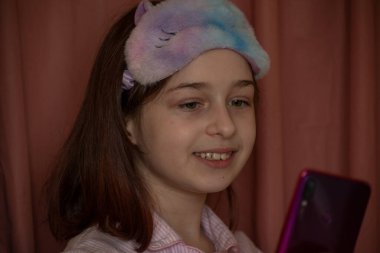 İnsanlar ve eğlence konsepti. Kırmızı ceketli bir kız selfie çekiyor. Evinde elinde telefon olan 9 yaşında bir kız. Pijamalı bir genç. Ev elbiseli küçük kız..