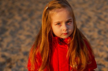 Kumsalda kumsalda yürüme yolu akşam güneşinde. Nehrin sonunda, kırmızı ceketli küçük bir kız. Eski model. Kırmızı ceketli küçük bir kız doğada yürüyor. Kum nehri. Portre