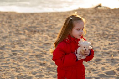 Kumsalda kumsalda yürüme yolu akşam güneşinde. Nehrin sonunda, kırmızı ceketli küçük bir kız. Eski model. Kırmızı ceketli küçük bir kız doğada yürüyor. Kum nehri. Portre
