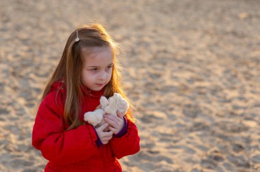 Kumsalda kumsalda yürüme yolu akşam güneşinde. Nehrin sonunda, kırmızı ceketli küçük bir kız. Eski model. Kırmızı ceketli küçük bir kız doğada yürüyor. Kum nehri. Portre