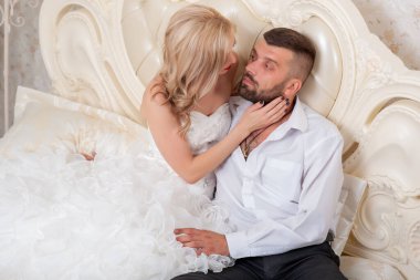 Yatakta dinlenen genç ve güzel bir çift. Gelin ve damat yataktalar. Düğün günlerinde genç bir aile. Gelinlik. Sakallı damat. Sevgi. Beyaz elbiseli. Sarışın ve esmer. Bir aile. Düğün.