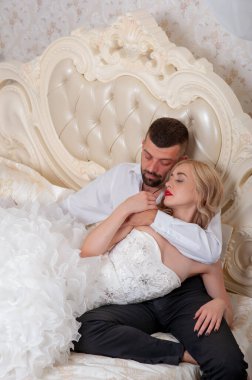 Yatakta dinlenen genç ve güzel bir çift. Gelin ve damat yataktalar. Düğün günlerinde genç bir aile. Gelinlik. Sakallı damat. Sevgi. Beyaz elbiseli. Sarışın ve esmer. Bir aile. Düğün.