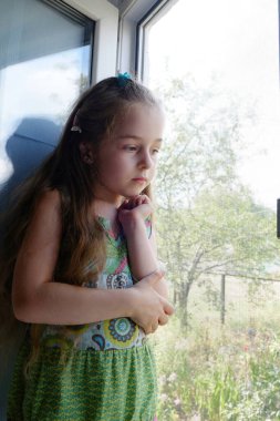 Pencerenin yanındaki küçük kız. Evde pencerenin yanında oturan 5 yaşında bir kız çocuğu. Çocukluk, çocuk, pencere. Evde kal.