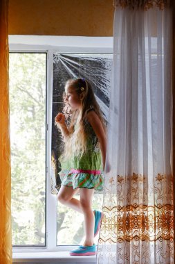 Pencerenin yanındaki küçük kız. Evde pencerenin yanında oturan 5 yaşında bir kız çocuğu. Çocukluk, çocuk, pencere. Evde kal.
