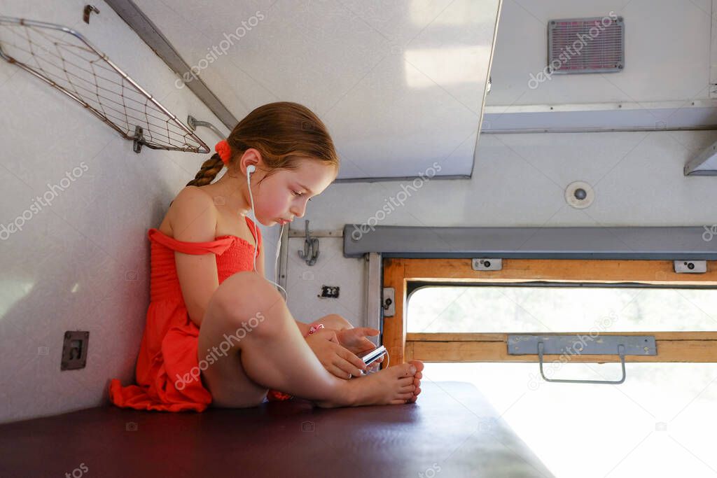 Cute girl lying on the top shelf in the train. Summer Vacation and Travel Concept. the girl in the train lies on the top shelf. A girl of 5 or 6 years old rides on a train. Teen travels. Smartphone