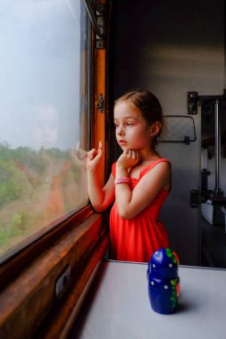 Cute girl in the train. Summer Vacation and Travel Concept. A girl of 5 or 6 years old rides on a train. Teen travels. Little girl with long hair. Child portrait clipart