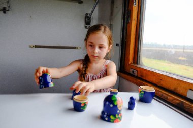 Trendeki tatlı kız. Yaz Tatili ve Seyahat Konsepti. 5-6 yaşlarında bir kız trene biniyor. Gençler seyahat eder. Uzun saçlı küçük kız. Çocuk portresi