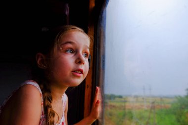 Cute girl in the train. Summer Vacation and Travel Concept. A girl of 5 or 6 years old rides on a train. Teen travels. Little girl with long hair. Child portrait
