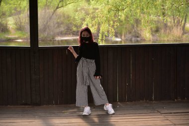 Dışarıdaki koruyucu maskeli kadın. Dışarıdaki maskeli kız. Virüs, maske, bahar. Kız 9 yaşında. Sokak. Virüs ve bakterilere karşı koruma. Tıbbi solunum maskesi. Salgın hastalık. Koruma