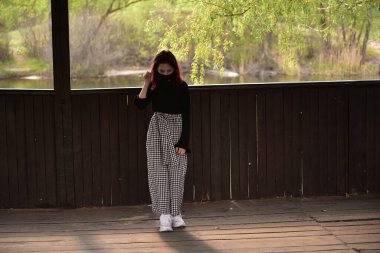 Dışarıdaki koruyucu maskeli kadın. Dışarıdaki maskeli kız. Virüs, maske, bahar. Kız 9 yaşında. Sokak. Virüs ve bakterilere karşı koruma. Tıbbi solunum maskesi. Salgın hastalık. Koruma