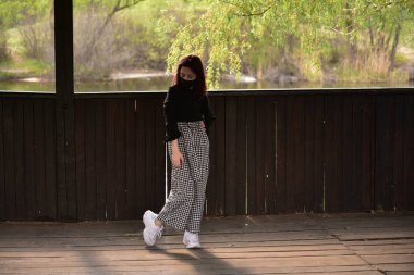 Dışarıdaki koruyucu maskeli kadın. Dışarıdaki maskeli kız. Virüs, maske, bahar. Kız 9 yaşında. Sokak. Virüs ve bakterilere karşı koruma. Tıbbi solunum maskesi. Salgın hastalık. Koruma