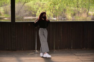 Dışarıdaki koruyucu maskeli kadın. Dışarıdaki maskeli kız. Virüs, maske, bahar. Kız 9 yaşında. Sokak. Virüs ve bakterilere karşı koruma. Tıbbi solunum maskesi. Salgın hastalık. Koruma