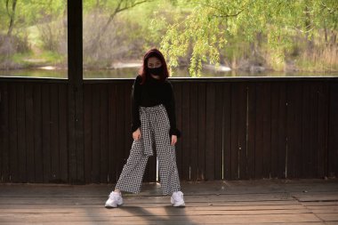 Dışarıdaki koruyucu maskeli kadın. Dışarıdaki maskeli kız. Virüs, maske, bahar. Kız 9 yaşında. Sokak. Virüs ve bakterilere karşı koruma. Tıbbi solunum maskesi. Salgın hastalık. Koruma