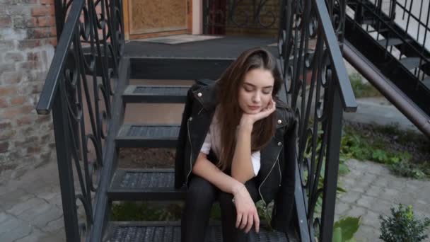 少女の肖像画 その美しいスタイリッシュな女の子はカントリーハウスのしきい値に座っています 女の子は家の前のポーチの階段に座っている 入口の階段に女性が座っている — ストック動画