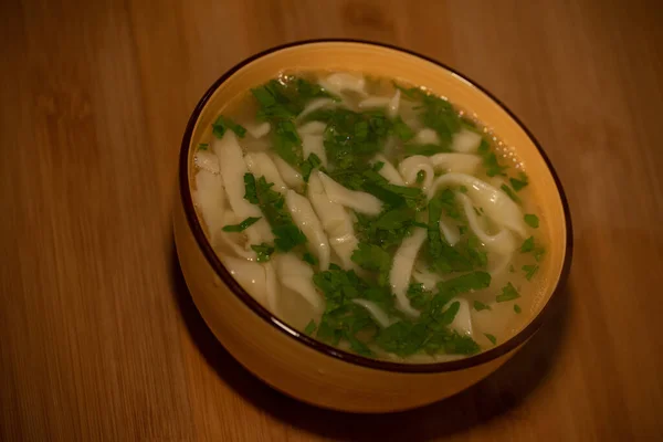 Chicken Noodle Soup. Chicken and noodle soup on an orange tablecloth in an orange plate. Food photography. Hot dish. Broth with noodles. Chicken, noodles. Homemade noodles and broth. Dill and parsley