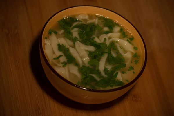 Chicken Noodle Soup. Chicken and noodle soup on an orange tablecloth in an orange plate. Food photography. Hot dish. Broth with noodles. Chicken, noodles. Homemade noodles and broth. Dill and parsley