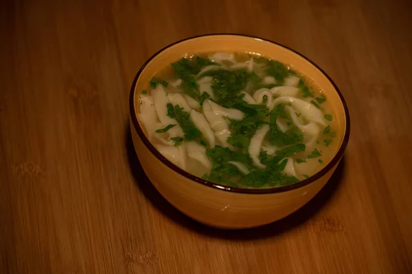 Chicken Noodle Soup. Chicken and noodle soup on an orange tablecloth in an orange plate. Food photography. Hot dish. Broth with noodles. Chicken, noodles. Homemade noodles and broth. Dill and parsley