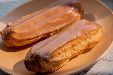 Kremalı kremalı kremalı kek. Üzerine kahverengi ve beyaz şekerli krema dökülmüş muhallebi kekleri. Çay ya da kahve için tatlı ikramları. Yakın plan. Seçici odaklanma. Kremalı pasta. Tatlı. Bej bir tabakta dört kek