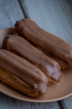 Kremalı kremalı kremalı kek. Üzerine kahverengi ve beyaz şekerli krema dökülmüş muhallebi kekleri. Çay ya da kahve için tatlı ikramları. Yakın plan. Seçici odaklanma. Kremalı pasta. Tatlı. Bej bir tabakta dört kek