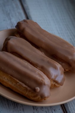 Kremalı kremalı kremalı kek. Üzerine kahverengi ve beyaz şekerli krema dökülmüş muhallebi kekleri. Çay ya da kahve için tatlı ikramları. Yakın plan. Seçici odaklanma. Kremalı pasta. Tatlı. Bej bir tabakta dört kek