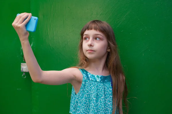 Yeşil arka planda akıllı telefon kullanan tatlı küçük kız. Küçük kız selfie çekiyor. Alfa Nesli Milenyum Çocukları - Etkin İnternet Kullanıcıları. Z nesli.