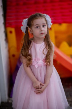 Pembe prenses elbisesi içinde beş yaşında tatlı bir kız. 5 yaşındaki mutlu sarışın bir kızın portresi. İki at kuyruklu ve beyaz kurdeleli küçük kız. Çocuk