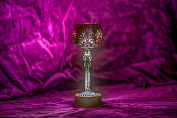 Close up of an illuminated red bohemian crystal wine glass with velvet background
