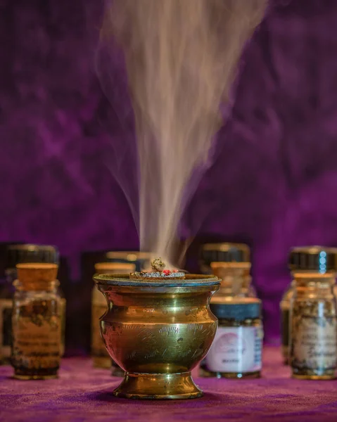 Smoke of burning white sage on an incense burner with more little bottles in the background