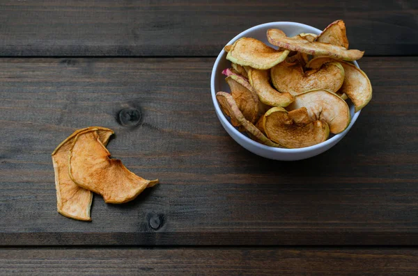 Chips of fresh apples with cinnamon are on a white plate on a background of black wooden boards. Organic apple chips. Dried fruits. Healthy sweet snack.