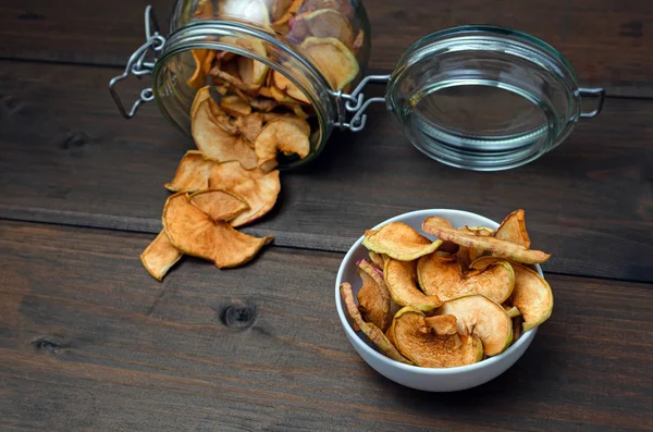 Healthy homemade sweet dehydrated and raw organic apple chips in a plate and glass jar on the wooden table background with copy space. — Stock Photo, Image