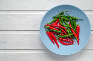 Modern Arkaplanda Red Hot Chili Peppers veya Yuvarlak mavi bir tabakta White table. Bir sürü kırmızı ve yeşil acı biber. Metnin için alanı kopyala. Düz yatış, üst görünüm.