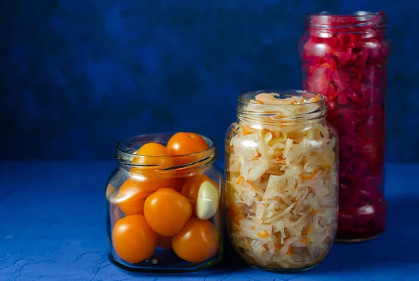 Çeşitli modern cam kavanozlarda kapanışa hazır turşulu sebzeler. Beyaz ve kırmızı pancar, lahana ve sarımsaklı sarı kiraz domatesli klasik mavi arka plan. — Stok fotoğraf