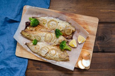 Fırın fırınında soğan halkalı uskumru, brokoli ve limon koyu ahşap arka planda mavi peçeteyle. Keto diyeti ve sağlıklı beslenme. Boşluğu kopyala