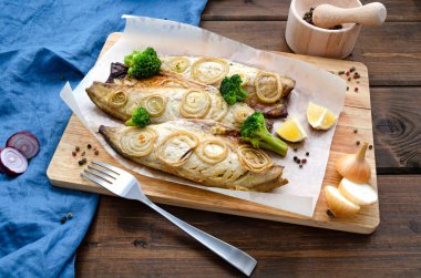 Fırında pişmiş taze uskumru doğranmış soğan halkaları brokoli ve limonla birlikte mavi peçete ve çatalla koyu ahşap bir zemin üzerinde. Keto diyeti ve sağlıklı beslenme. Boşluğu kopyala