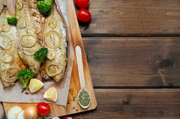 Close-up fresh tender baked mackerel in the oven with rings of chopped onion, broccoli, tomatoes and lemon on a dark wooden background. keto and flexitarian diet and healthy eating. — Stock fotografie