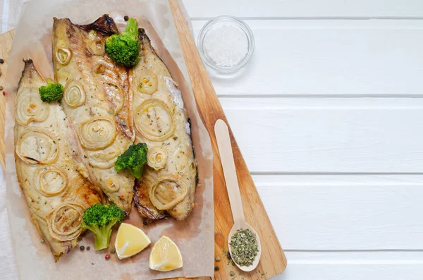 Fresh tender baked mackerel with rings of chopped onion, broccoli and lemon on a dark wooden cutting board in baking paper. keto and flexitarian diet and healthy eating. with copy space — Stock fotografie