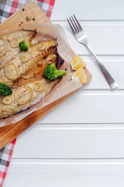 Detailní nabídka pečené makrely v troubě s kroužky nasekané cibule, brokolice, rajčat a citronu na bílém dřevěném pozadí s modrým ubrouskem a vidličkami. keto a flexitářská strava a zdravé stravování. — Stock fotografie