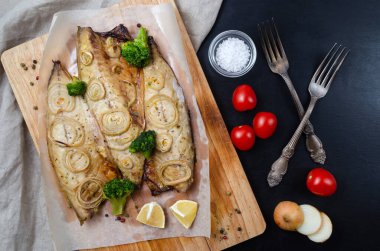 Fırında uskumru, doğranmış soğan, brokoli ve limon halkaları ve ahşap kesme tahtasının üzerinde siyah bir arkaplan. Keto ve fleksitrik diyet ve sağlıklı beslenme.